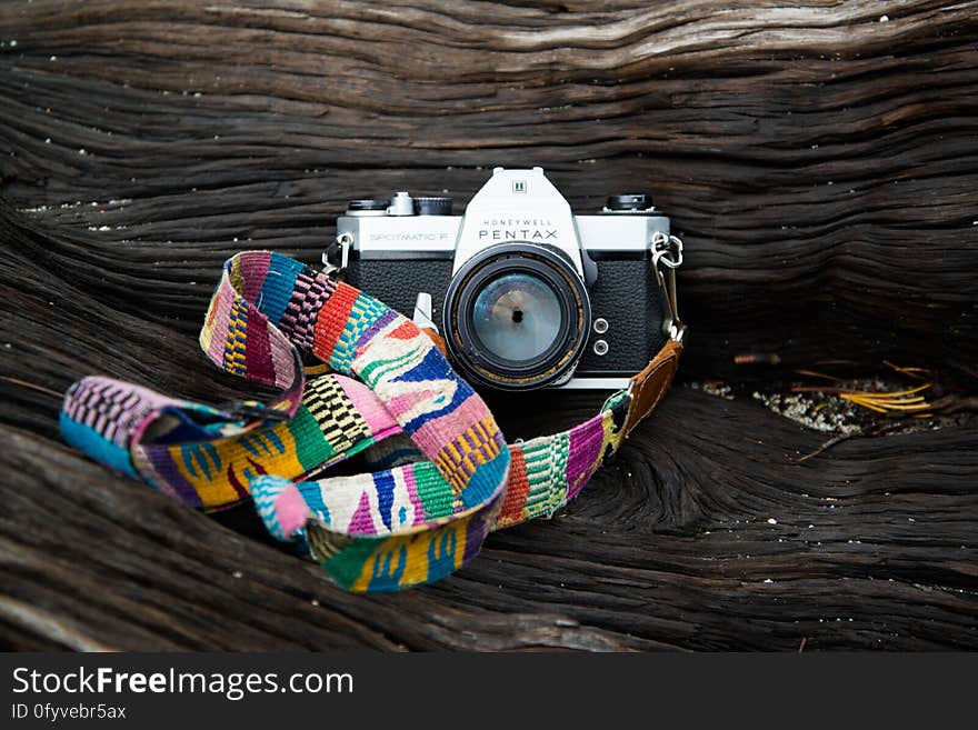 Pentax camera with colorful cloth strap on wooden log. Pentax camera with colorful cloth strap on wooden log.