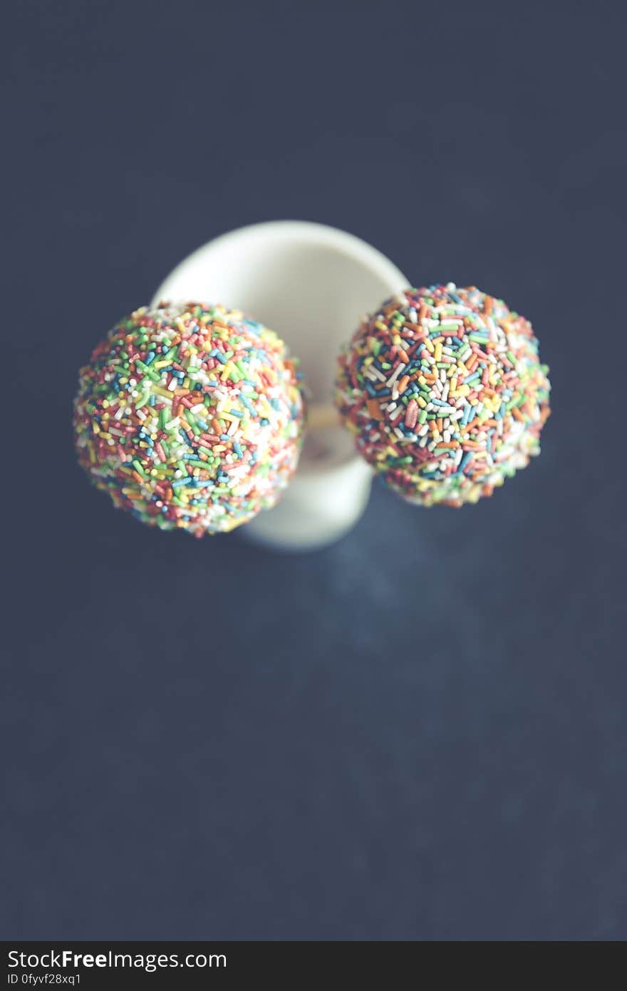 A pair of cake pops with colorful sprinkles.