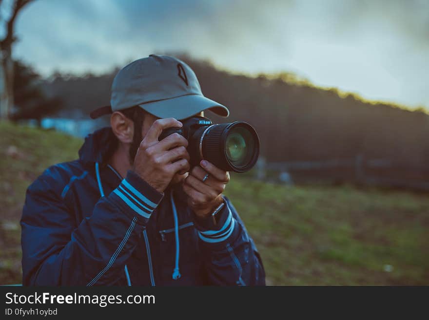 Man in baseball cap using professional camera outdoors at sunset. Man in baseball cap using professional camera outdoors at sunset.