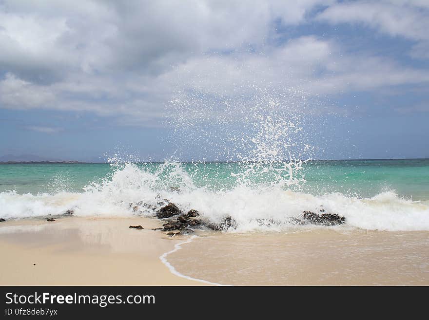 Waves splashing on rocks on sandy beach on sunny day. Waves splashing on rocks on sandy beach on sunny day.