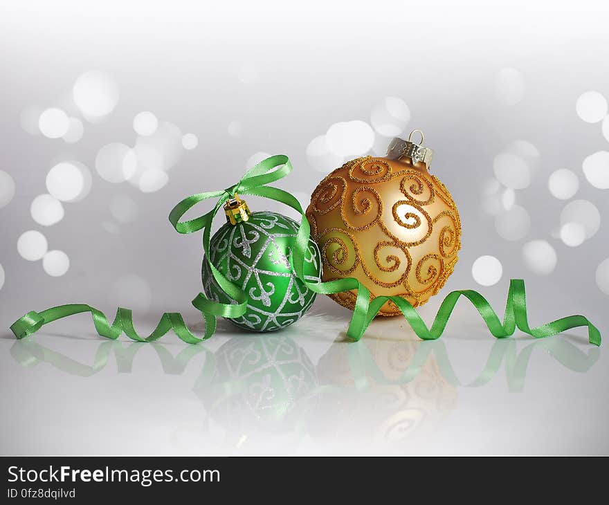 Green and gold Christmas tree ornament balls with green ribbon against white bokeh lights. Green and gold Christmas tree ornament balls with green ribbon against white bokeh lights.