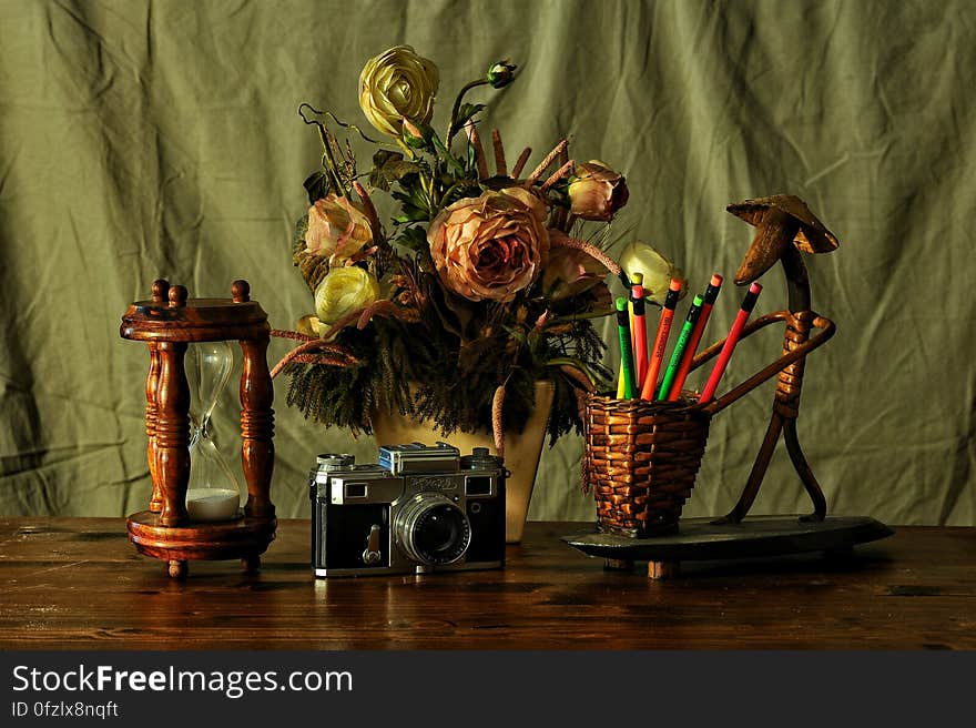 Still life on table top with timer, vase of (paper) roses, basket of colored pencils and retro film camera green curtain background. Still life on table top with timer, vase of (paper) roses, basket of colored pencils and retro film camera green curtain background.