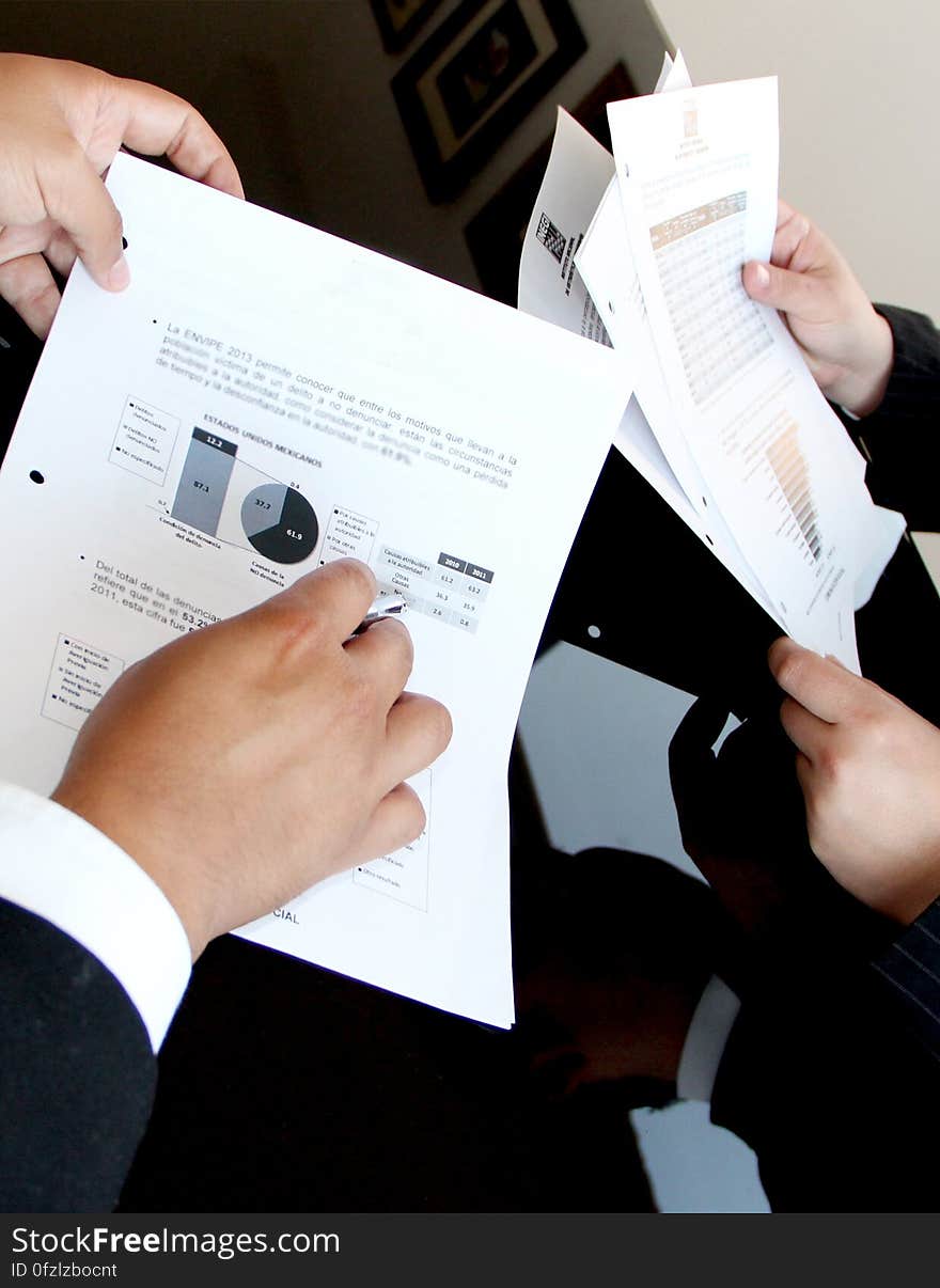 Close up of hands of business professionals holding documents with charts and information. Close up of hands of business professionals holding documents with charts and information.