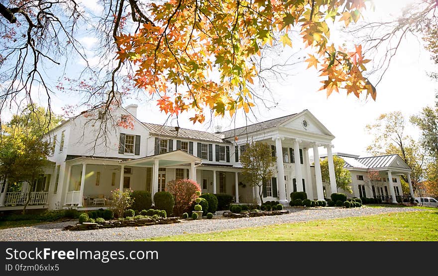 Exterior of white estate home with green lawn on sunny day. Exterior of white estate home with green lawn on sunny day.