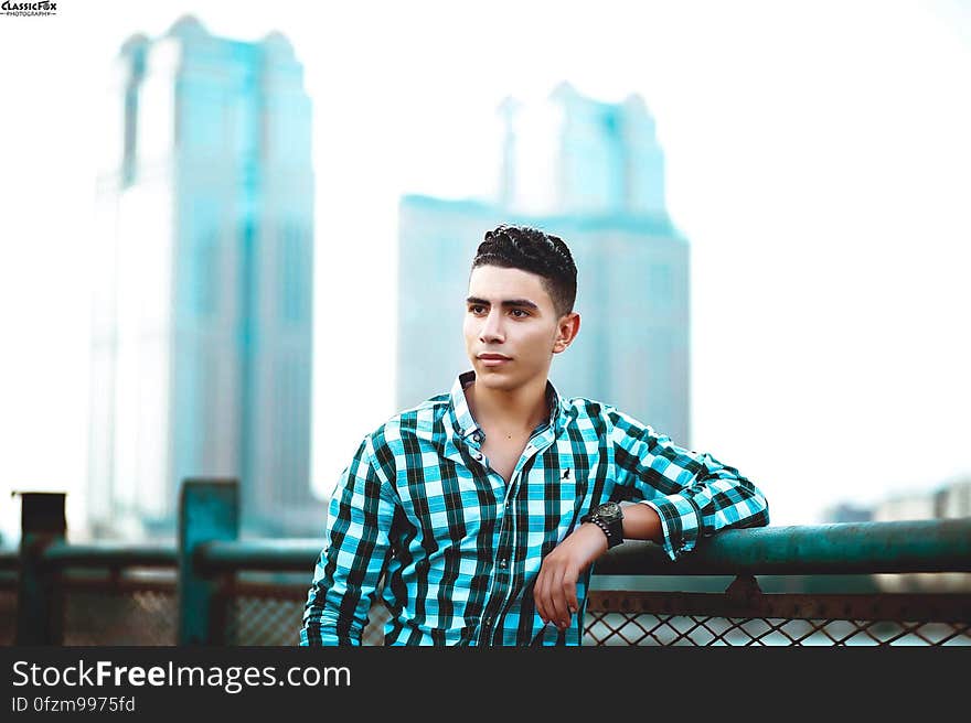 A young man leaning on a fence in the city.