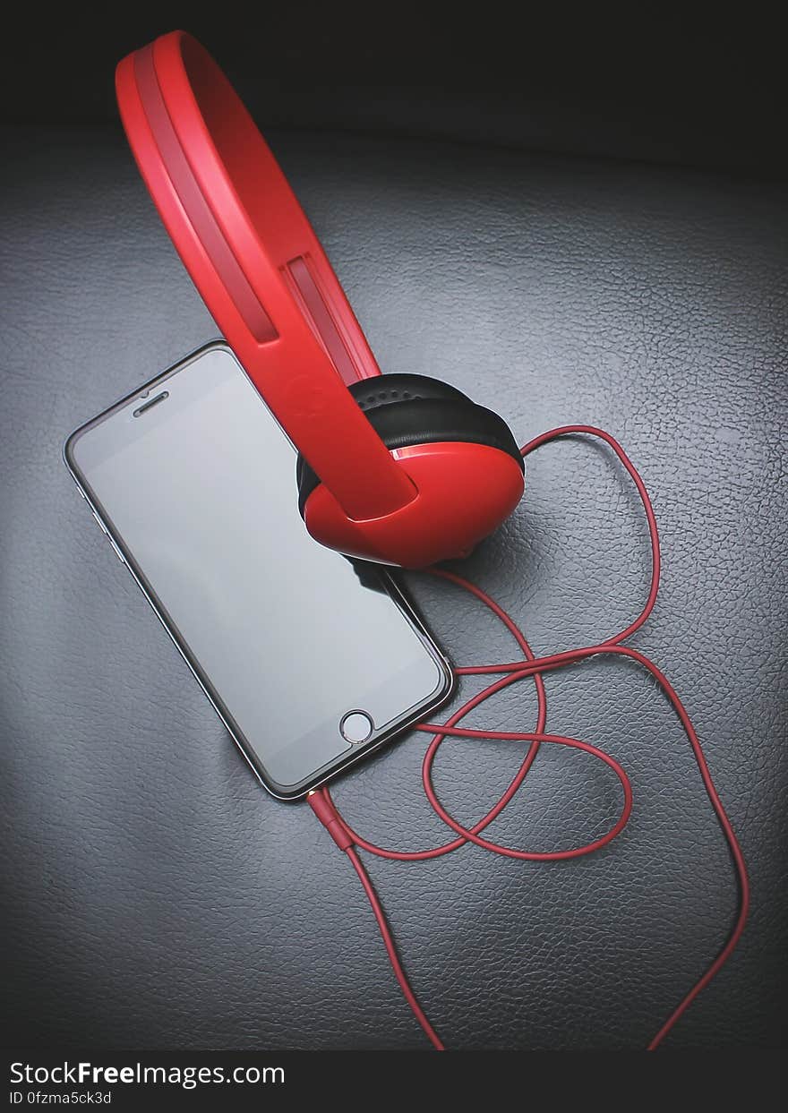 Red headphones attached to cell phone on grey leather. Red headphones attached to cell phone on grey leather.