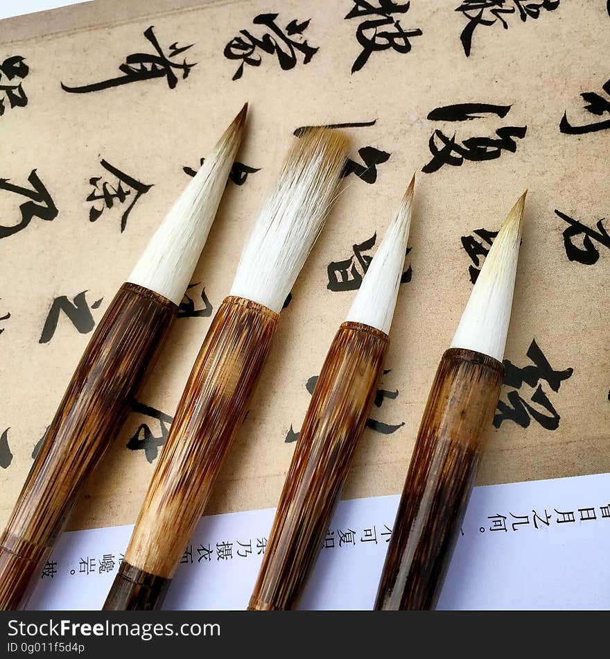 Close up of art brushes with wooden handles on parchment paper with Chinese characters. Close up of art brushes with wooden handles on parchment paper with Chinese characters.