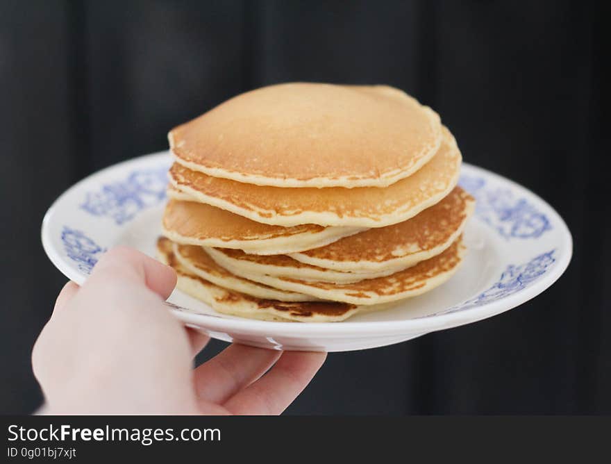 A person holding out a plate of thick American style pancakes. A person holding out a plate of thick American style pancakes.