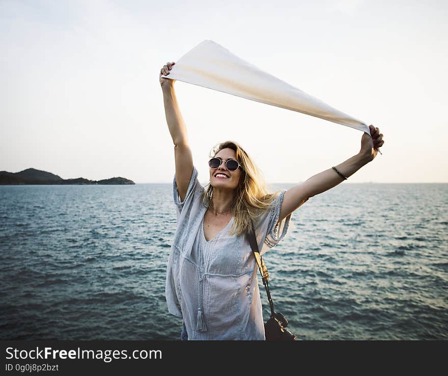 Smiling blond woman in pale blue dress with her arms outstretched holding a piece of white material, background of sea and waves. Smiling blond woman in pale blue dress with her arms outstretched holding a piece of white material, background of sea and waves.