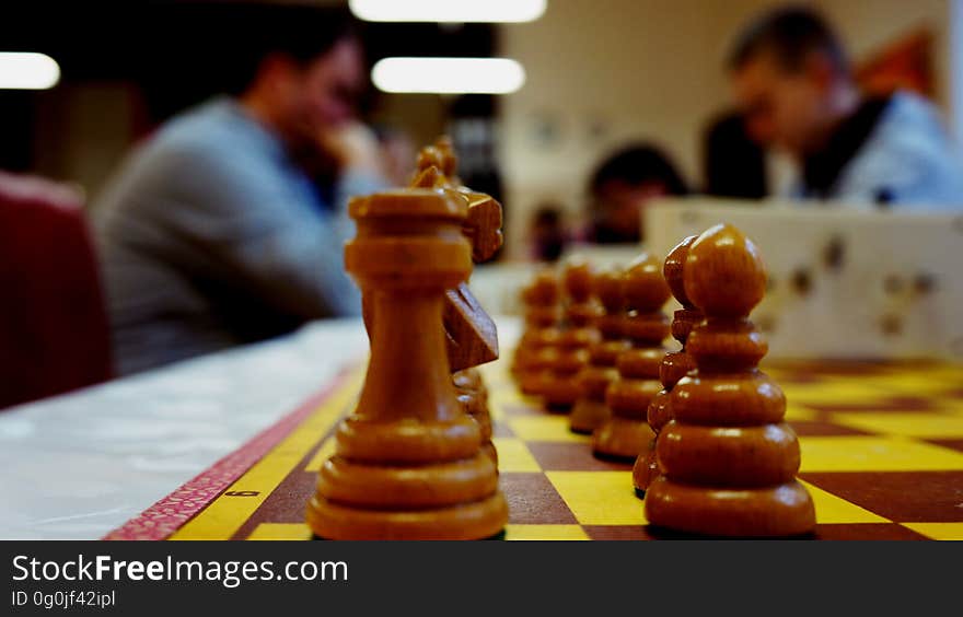 A close up of a chess board with chess players on the background.