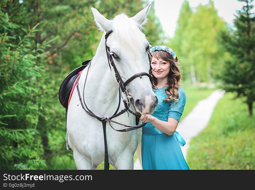 Outdoor portrait of a big gray horse and a Caucasian smiling woman in a blue dress in the forest. Outdoor portrait of a big gray horse and a Caucasian smiling woman in a blue dress in the forest.