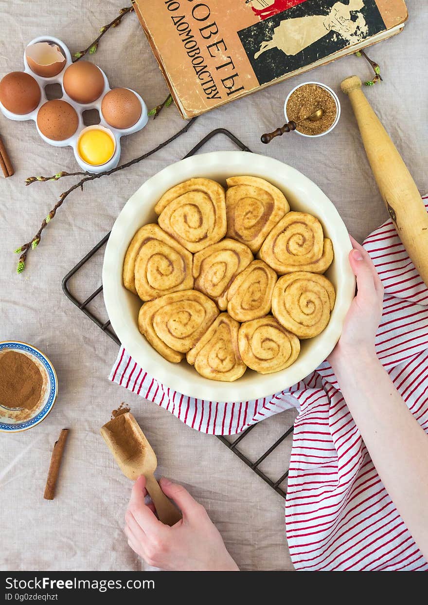 Still life on unbaked cinnamon rolls in pan with ingredients and cookbook on countertop.