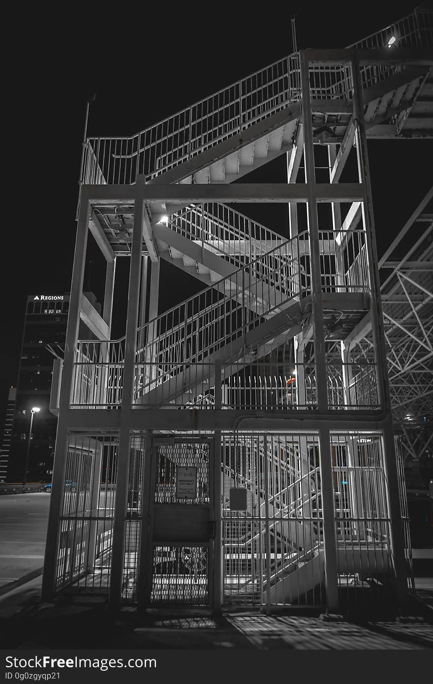 External stairway (emergency fir exit) with metal rails and metal door with bars seen under street lighting, black starless sky. External stairway (emergency fir exit) with metal rails and metal door with bars seen under street lighting, black starless sky.