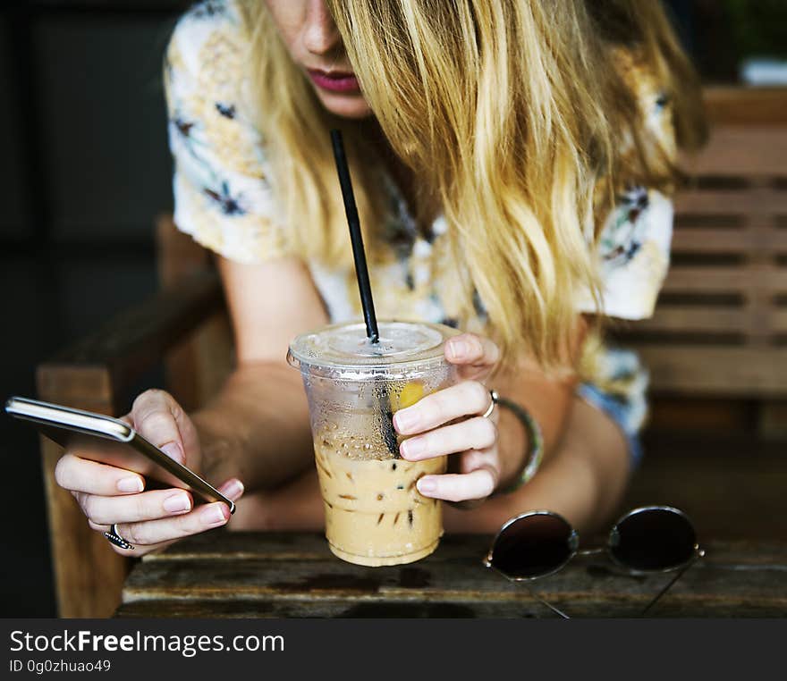 A woman reading her mobile phone while drinking an iced coffee. A woman reading her mobile phone while drinking an iced coffee.