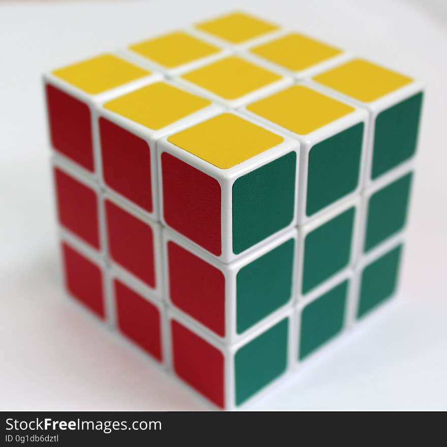 Rubik's cube with three faces showing, top has nine yellow squares, sides have nine gray and nine red squares, bright background. Rubik's cube with three faces showing, top has nine yellow squares, sides have nine gray and nine red squares, bright background.