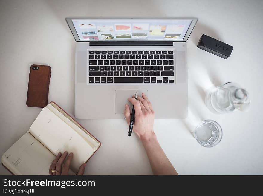 A person writing on his notebook or journal while working on a laptop seen from above. A person writing on his notebook or journal while working on a laptop seen from above.