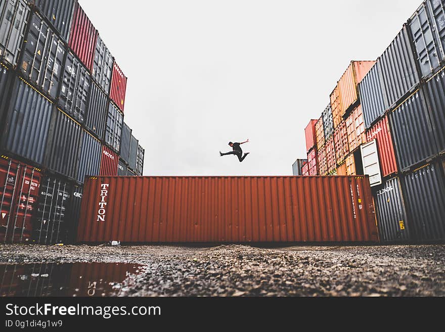 Athlete jumping high over one of a collection of containers used for export and import of goods by ship or rail, pale gray sky background. Athlete jumping high over one of a collection of containers used for export and import of goods by ship or rail, pale gray sky background.