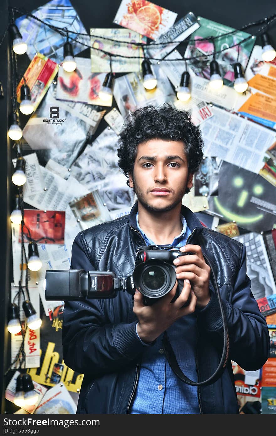 A man taking a selfie through a mirror with background of lights and newspaper clippings. A man taking a selfie through a mirror with background of lights and newspaper clippings.