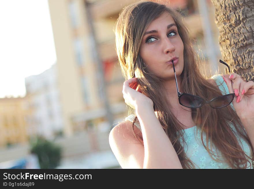 Woman Wearing Teal Floral Tank Top Holding Black Framed Sunglasses Near Tree Posing for a Picture during Daytime