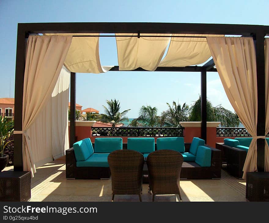 A pergola-style gazebo with curtains and chairs on a terrace. A pergola-style gazebo with curtains and chairs on a terrace.