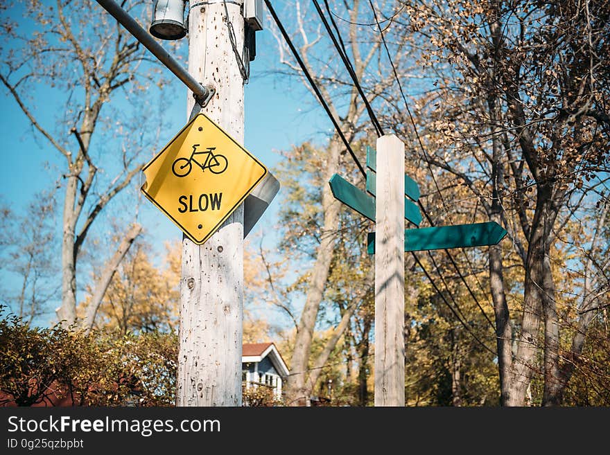 Yellow sign nailed to wooden post with text "slow" in uppercase black letters and the sign includes an image of a cycle, blue sky background. Yellow sign nailed to wooden post with text "slow" in uppercase black letters and the sign includes an image of a cycle, blue sky background.