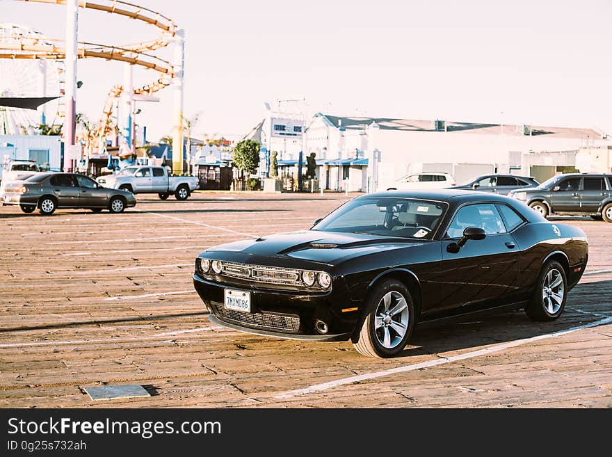 A muscle car on a parking lot with an amusement park on the background.