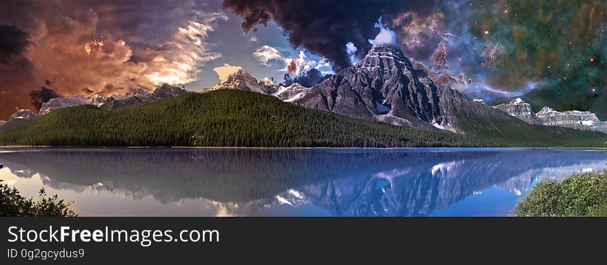 Mountain beside placid lake at dawn with dramatic orange and white clouds and blue sky and reflections in the lake. Mountain beside placid lake at dawn with dramatic orange and white clouds and blue sky and reflections in the lake.