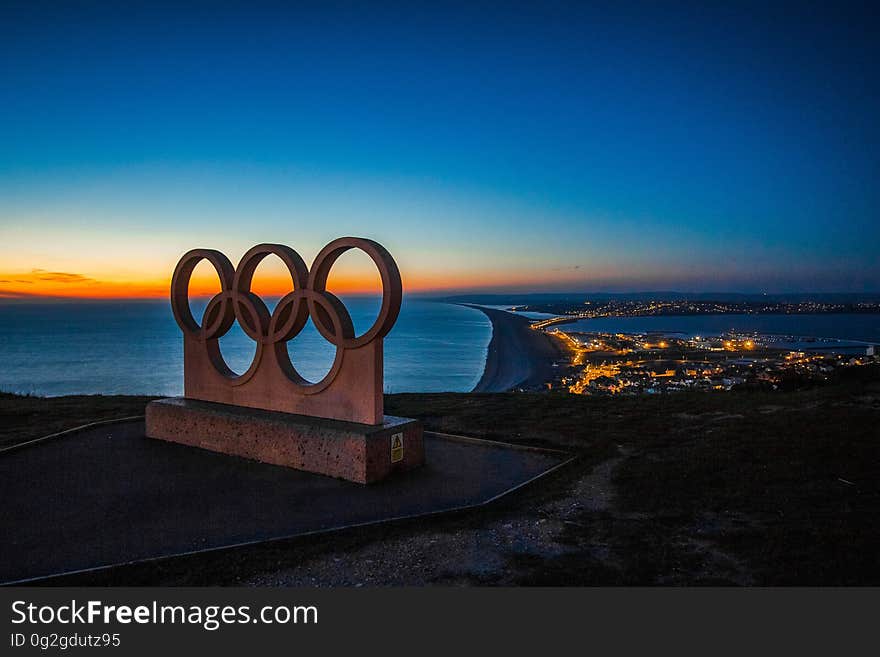 The olympic rings on a hill overlooking a city at night.