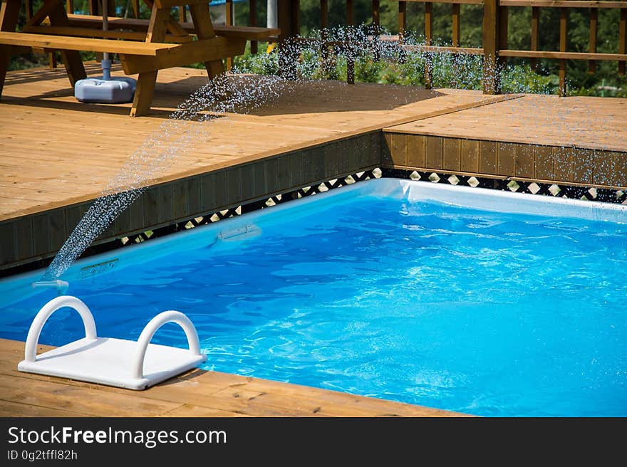 Fountain spraying in backyard swimming pool on sunny day. Fountain spraying in backyard swimming pool on sunny day.