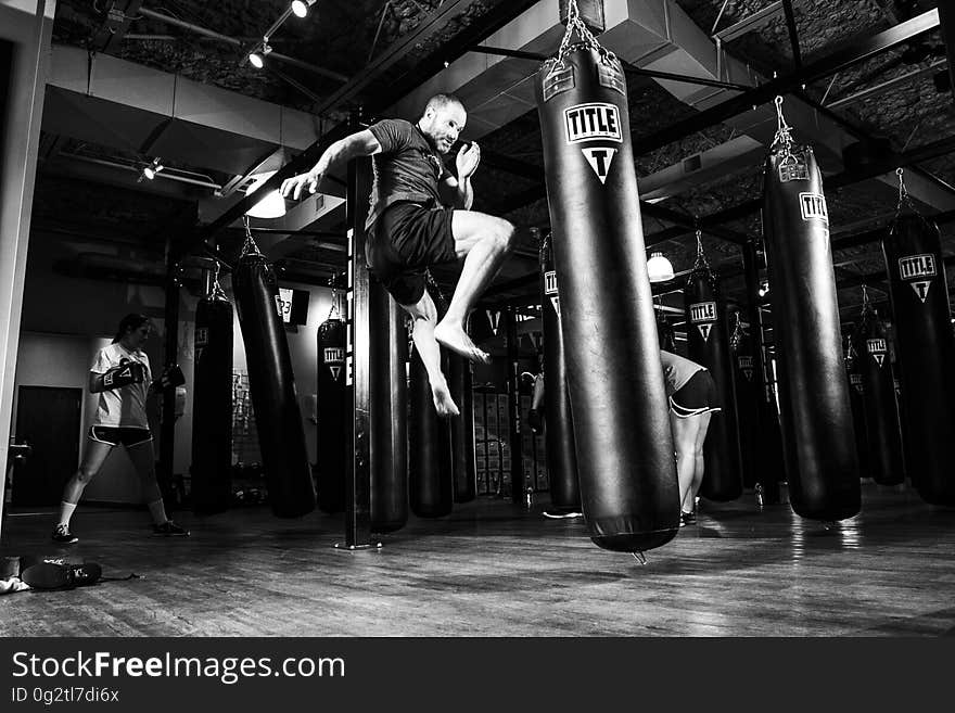 Man practicing kick boxing against bag inside gym in black and white. Man practicing kick boxing against bag inside gym in black and white.