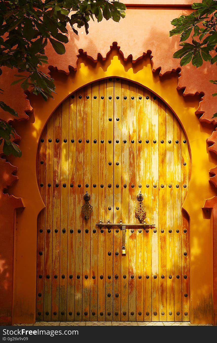 Golden vintage keyhole shaped door made of wooden planking with rows of large headed nails (bolts) decorating the door along with a long metal bolt and unusual handles hanging down. Golden vintage keyhole shaped door made of wooden planking with rows of large headed nails (bolts) decorating the door along with a long metal bolt and unusual handles hanging down.