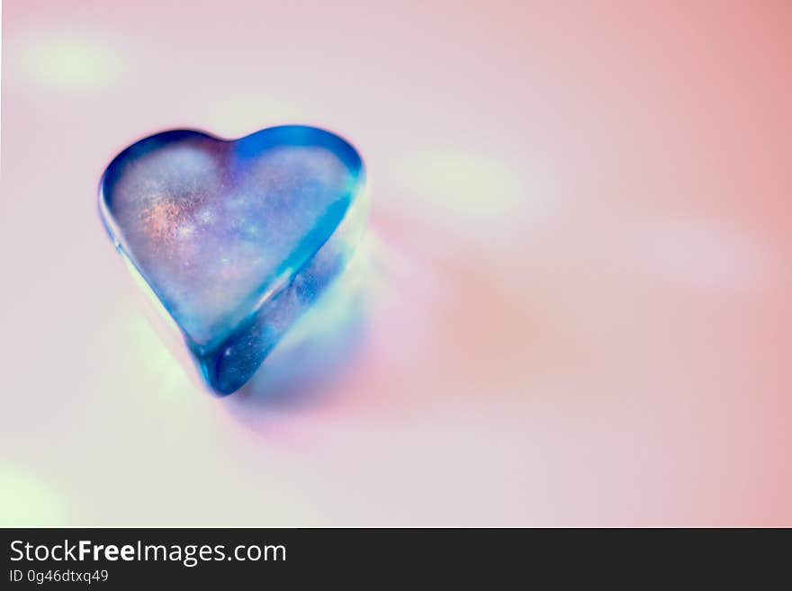 Close up of blue glass heart shaped ornament on pink. Close up of blue glass heart shaped ornament on pink.