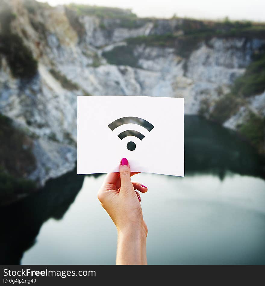 A woman holding up a paper with cut-out wifi sign against the rocky landscape.