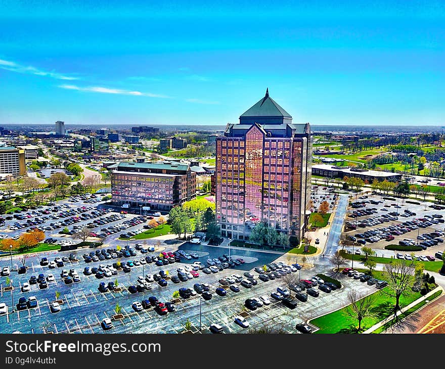 Aerial view of high rise building surrounded by parking lot against blue skies on sunny day.