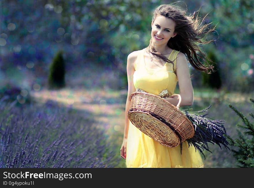 Woman in Yellow Maxi Dress Holding Brown Woven Picnic Basket Walking During Daytime