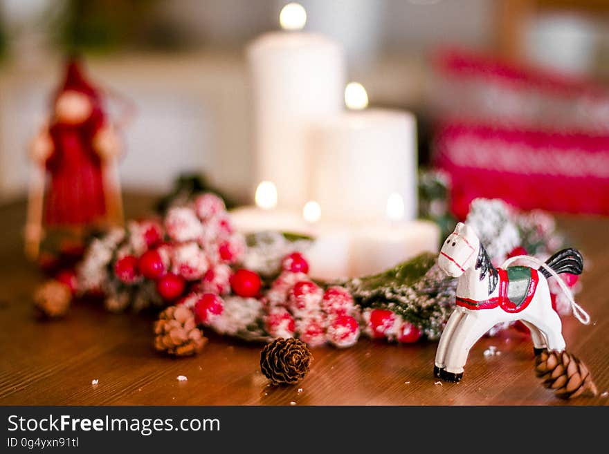 Christmas ornaments around white candles with pine cones on wooden table.