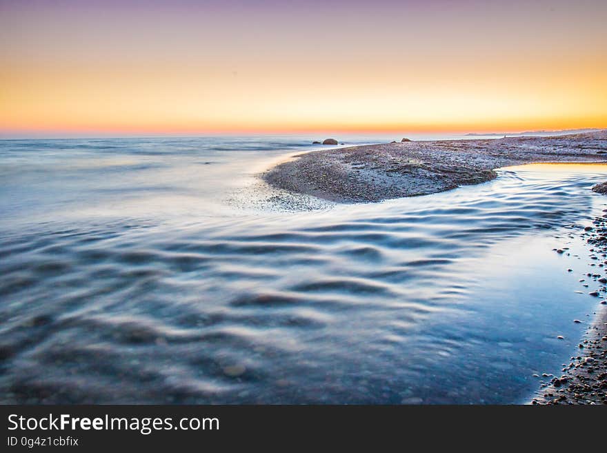 Waves on sandy beach at sunset.