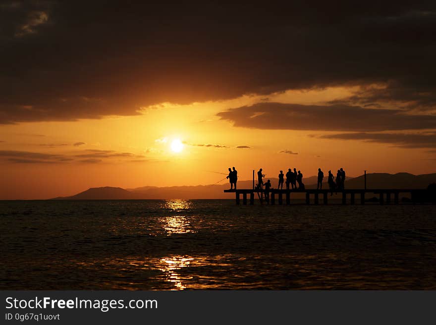 Silhouette of people standing on platform along waterfront at sunset. Silhouette of people standing on platform along waterfront at sunset.