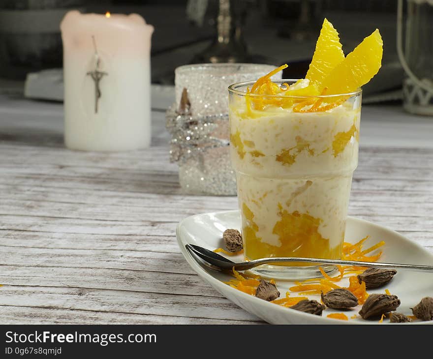 Breakfast fruit parfait in clear glass on white plate with oranges and nuts on rustic tabletop with candles. Breakfast fruit parfait in clear glass on white plate with oranges and nuts on rustic tabletop with candles.