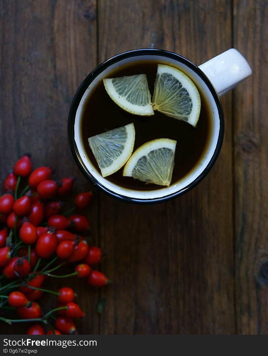 Flat lay of white mug with hot tea and lemon slices next to berries on rustic wooden boards. Flat lay of white mug with hot tea and lemon slices next to berries on rustic wooden boards.