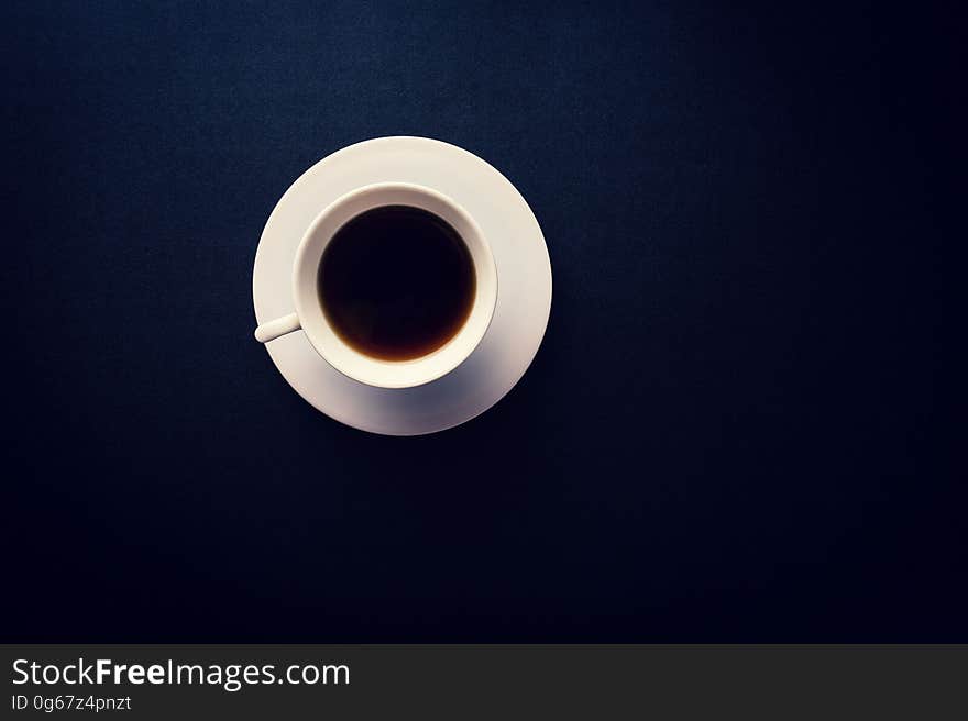 Flat lay overhead of white cup and saucer with coffee on black. Flat lay overhead of white cup and saucer with coffee on black.