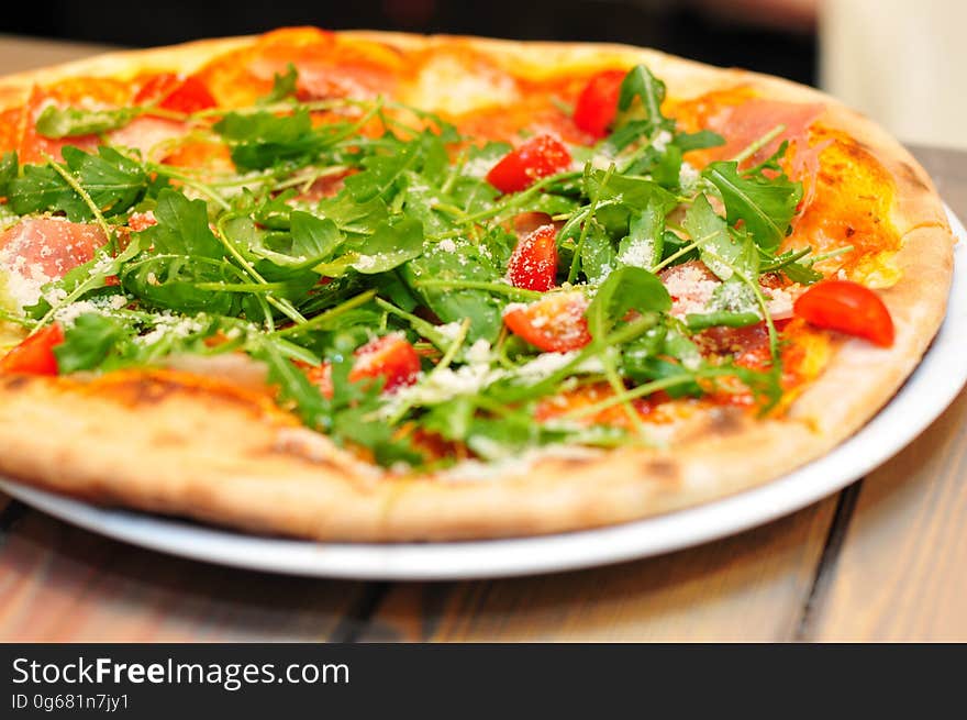 A close up of a pizza with rocket and cherry tomatoes on top. A close up of a pizza with rocket and cherry tomatoes on top.