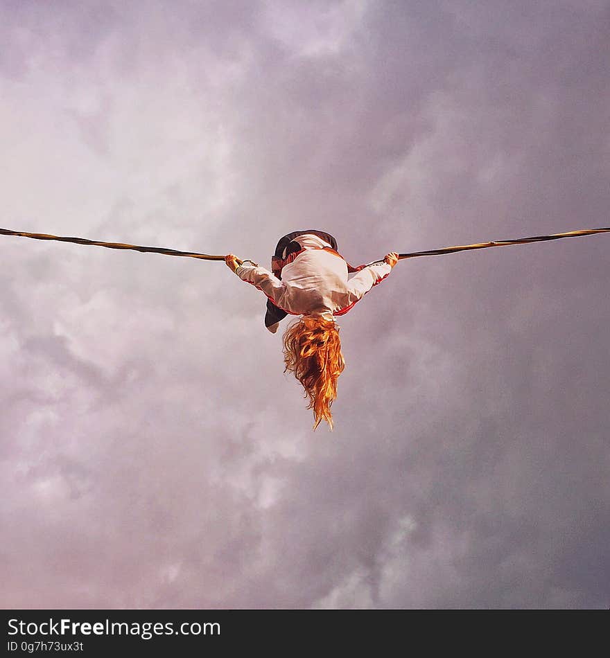 Person dangling over rope against grey clouds in overcast skies. Person dangling over rope against grey clouds in overcast skies.