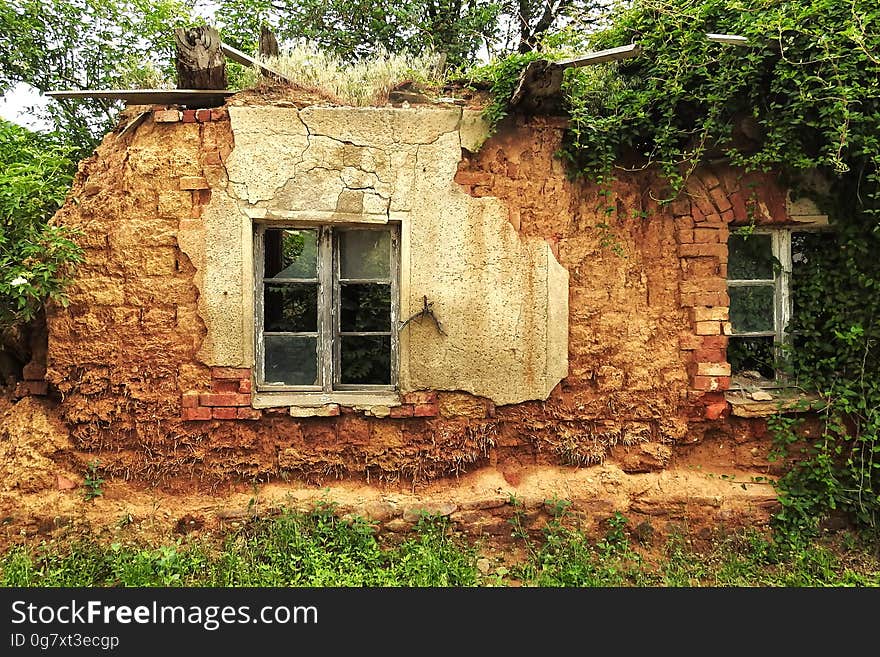 Exterior of overgrown stone house abandoned in weeds and trees.