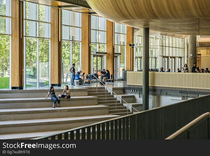 People on steps inside modern contemporary building with glass windows in sunlight. People on steps inside modern contemporary building with glass windows in sunlight.