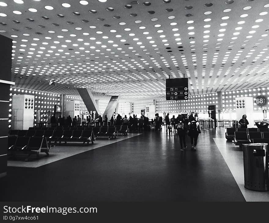 A black and white photo of people at a departure lounge at the airport. A black and white photo of people at a departure lounge at the airport.