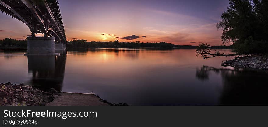 Under bridge spans over calm lake at sunset. Under bridge spans over calm lake at sunset.