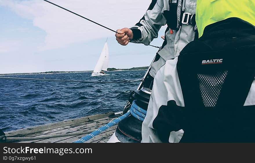 A man in a sailing jacket holding a cable on a sailboat. A man in a sailing jacket holding a cable on a sailboat.