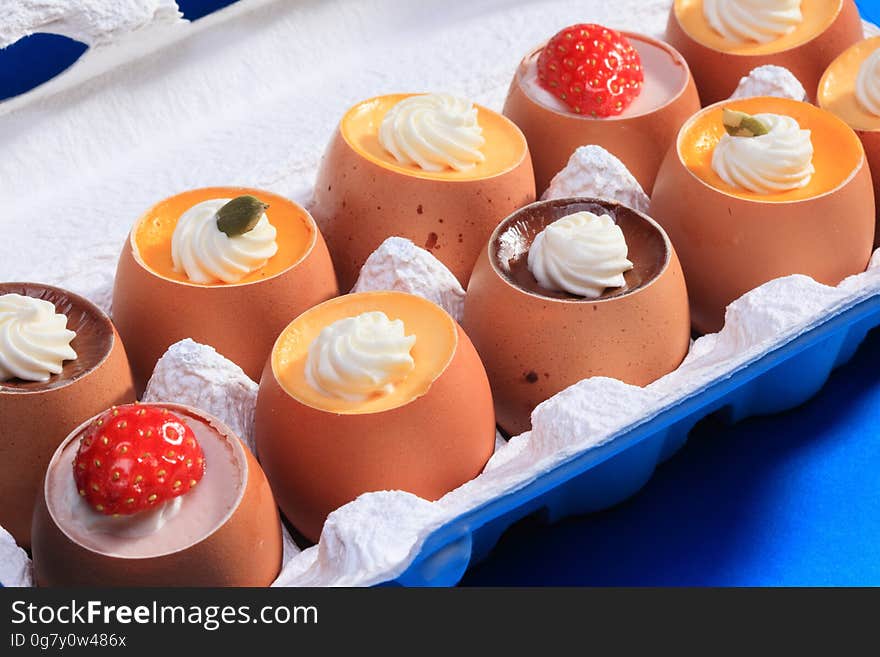 A close up of puddings in eggshells decorated with whipped cream and strawberries.