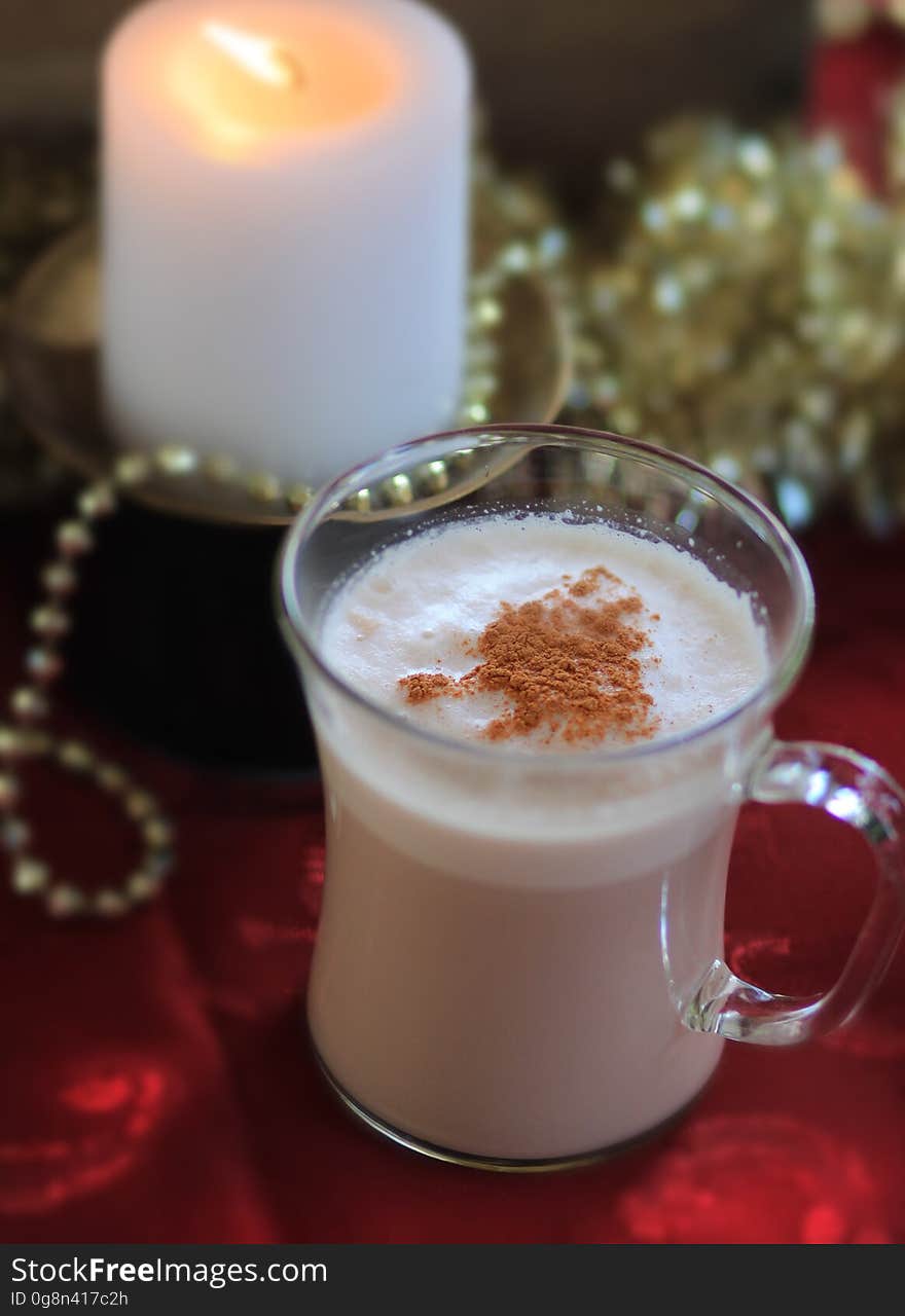 A hot drink in a glass with a candle in the background.